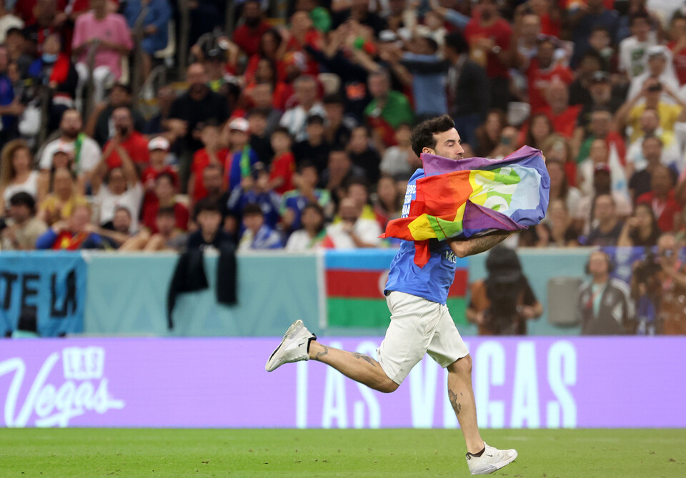 28일(현지시간) 카타르 루사일 스타디움에서 열린 2022 카타르 월드컵 조별리그 H조 2차전 포르투갈과 우루과이의 경기, 한 남성이 무지개 색깔의 깃발을 흔들며 경기장에 난입하고 있다. 이 남성이 입은 셔츠 뒤에는 'RESPECT FOR IRANIAN WOMAN'라고 적혀있다. [사진=뉴시스]