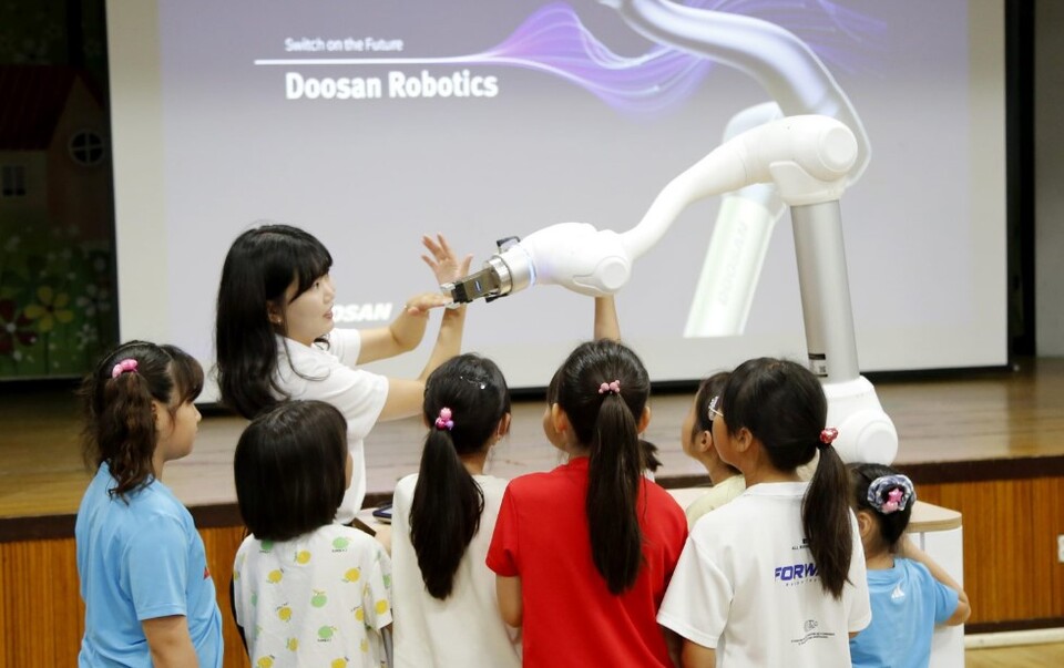 두산로보틱스 임직원이 아이들에게 협동로봇의 개념과 기본적인 작동 과정 등을 교육하고 있다. [사진=두산로보틱스]